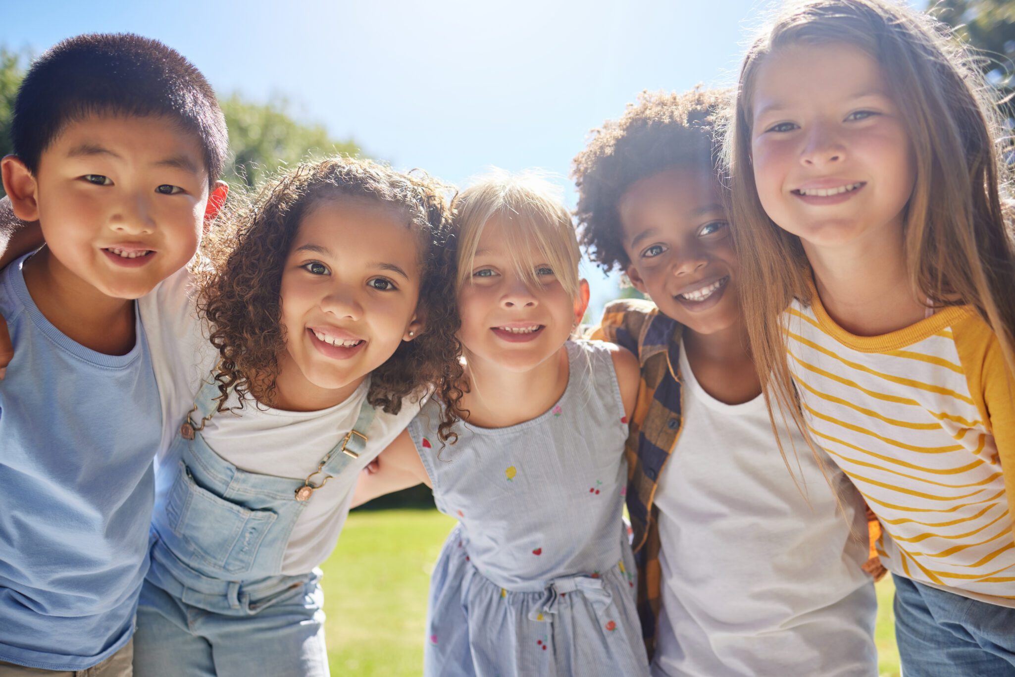 Happy, smile and portrait of kids in a park playing together outdoor in nature with friendship. Happiness, diversity and children friends standing, embracing and bonding in a outside green garden